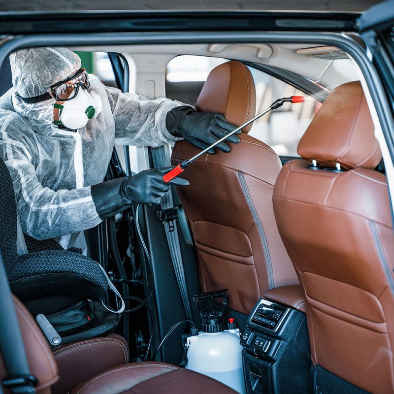 Disinfectant worker in protective mask and suit making disinfection of car seats